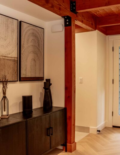 Modern entryway with wooden beams, a black sideboard, abstract wall art, decorative vases, and a glass door with a wreath leading outside.