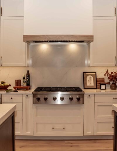 Modern kitchen with white cabinets, a stainless steel stove, marble backsplash, mixer, coffee maker, and decorative items on the countertop.