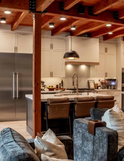 Modern open-concept kitchen and living space with exposed wooden beams, white cabinets, stainless steel appliances, and a central island with bar seating.