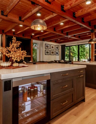 Modern kitchen with dark wood islands, white countertops, exposed wooden beams on the ceiling, pendant lights, and large windows providing natural light.
